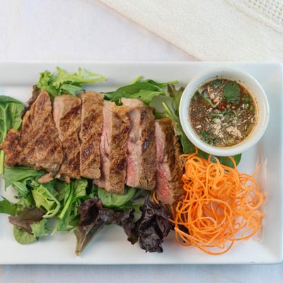 Sliced grilled steak with greens, shredded carrot, and dipping sauce.