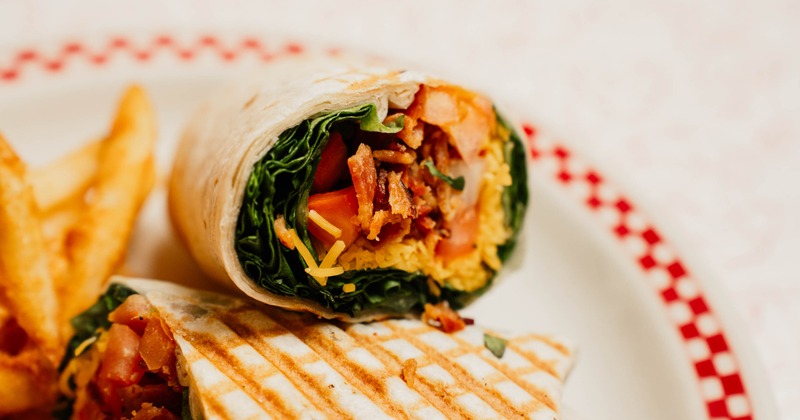 Wrap featuring grilled tortilla and various fillings, sliced in half, close-up
