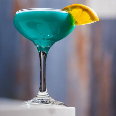Side view of a glass of the Blue Lagoon cocktail with lemon garnish.