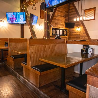 Dining room with wooden booths, tables, string lights and multiple televisions.