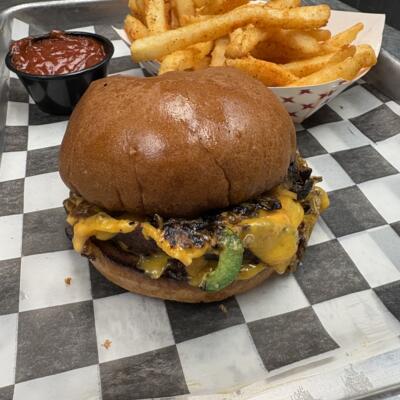 Cheeseburger with grilled vegetables and seasoned fries on checkered tray.