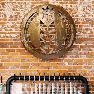 Metal brewery logo on the brick wall above beer taps.