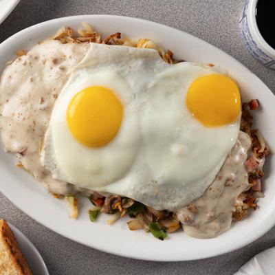 Stuffed hash browns with sausage gravy and fried eggs on a white plate.