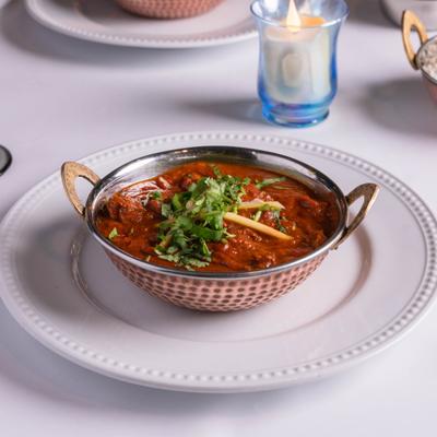 Punjabi Lamb Curry served in a traditional copper bowl on a white table.