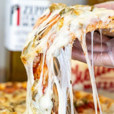 A close-up of a hand lifting a slice of pizza with melted cheese stretching.