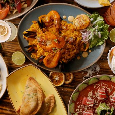 A colorful spread of seafood paella, empanadas, skewers, and red sauces.