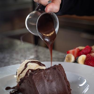 Chocolate cake with ice cream being topped with chocolate sauce.