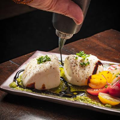 Burrata drizzled with oil beside colorful tomatoes.