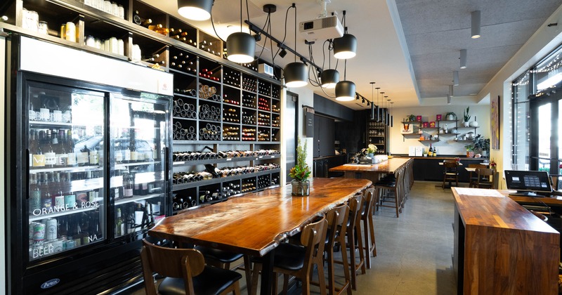 Bright wine bar interior - wall-to-wall wine racks, pendant lights, a long wooden communal table