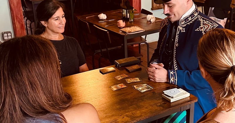A person in a top hat reading tarot cards to a group of people at a table