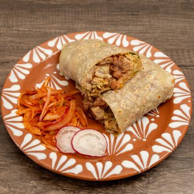 Pork belly burrito served with sauteed onions and radish slices on a patterned plate.
