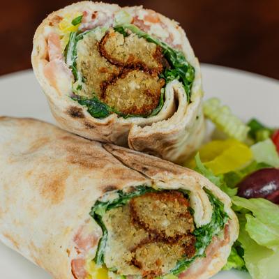 Falafel pita wrap sliced in half and served with salad on the side.