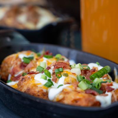 Loaded tater tots in a black skillet with sour cream, cheese, and scallions.