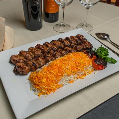 Beef kebab with saffron rice and charred tomatoes, accompanied by wine.