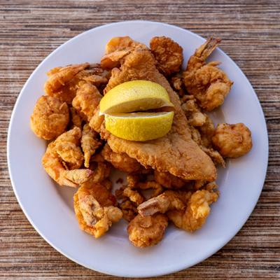 Fried seafood plate with shrimp, fish, scallops, clam strips, and lemon wedges.