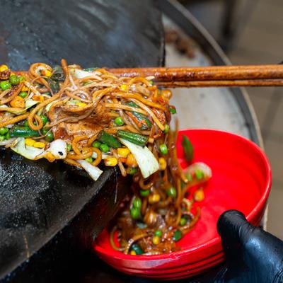 A dish of stir-fried noodles being served into a red bowl.