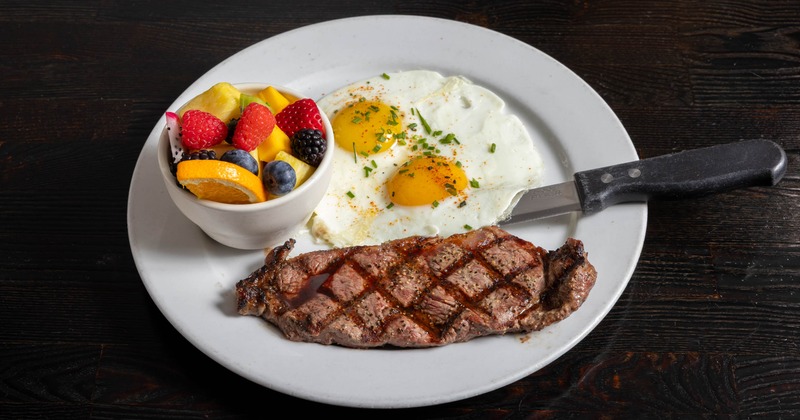 Steak and eggs served with fruit on a white plate
