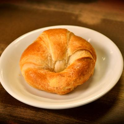 A croissant on a white saucer placed on a wooden table, close up.