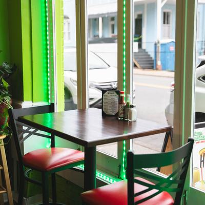 Two red bar stools and a table set with condiments sit by a window overlooking a street.
