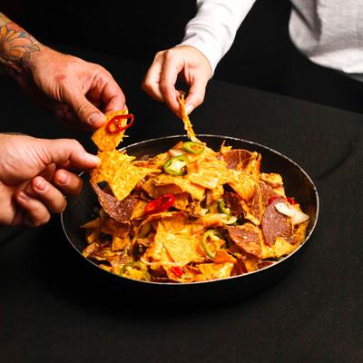 Nachos, with smoked pork belly, cheese, BBQ sauce, pickled peppers, and onions.