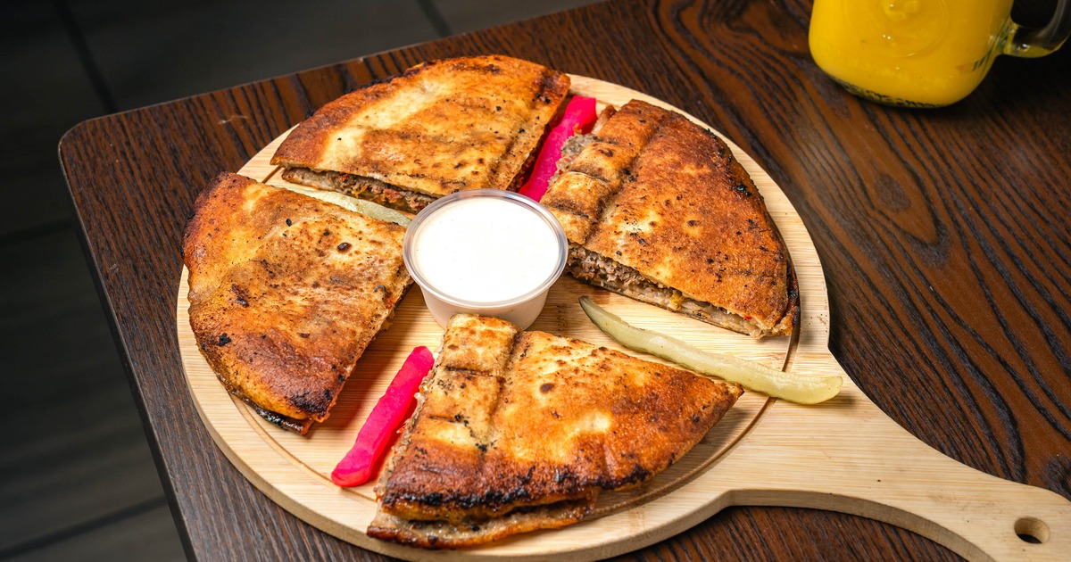 Round stuffed flatbread served with dip and pickles