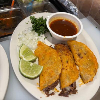Beef tacos served with consomme, lime wedges, diced onions and cilantro.