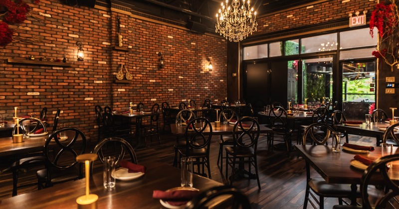 Interior dining area with brick walls, wooden tables, black chairs and a chandelier