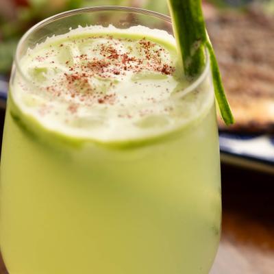Cocktail garnished with a fresh cucumber slice and a sprinkling of red chili spice.