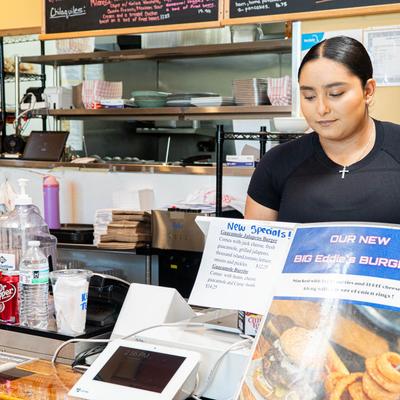 A cashier at a restaurant counter with menu specials.