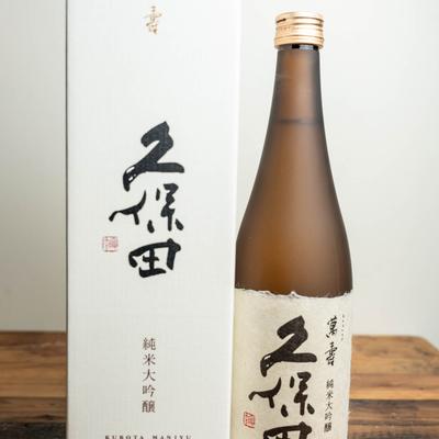 A brown  bottle of Kubota Senju sake with white label, and a white box next to it.