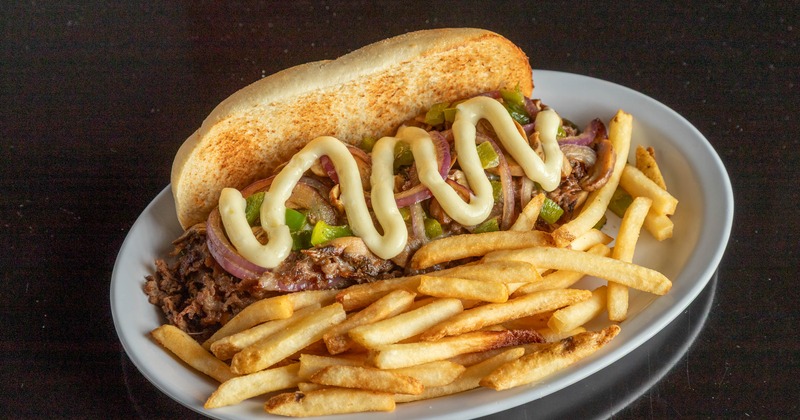 Philly cheesesteak sandwich served with fries on a white plate