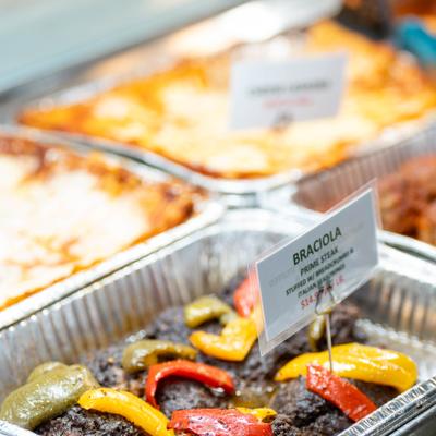 Buffet trays with braciola and pasta dishes with labels on display.