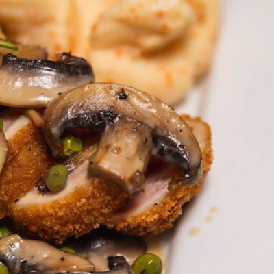 Close-up of Chicken Cordon Bleu topped with mushrooms and green peas.