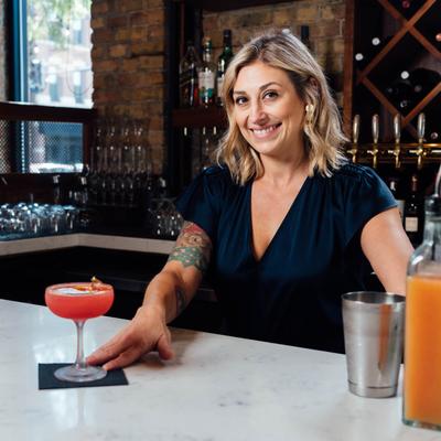 Bartender smiling and placing a red cocktail in a coupe glass on a bar