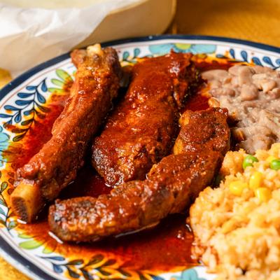 Pork ribs coated in sauce and served with rice and refried beans.