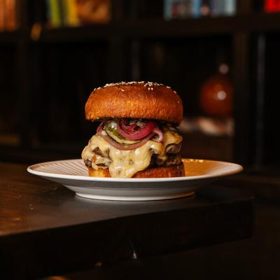 Burger topped with melted cheese and pickled onion, served on the table.