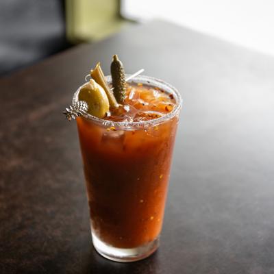 Bloody Mary in salt-rimmed glass, garnished with pickled vegetables on a skewer.