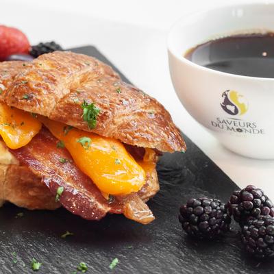 Croissant with cheddar, bacon, and a cup of coffee.