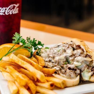Philly cheesesteak sandwich with seasoned fries and a soda.