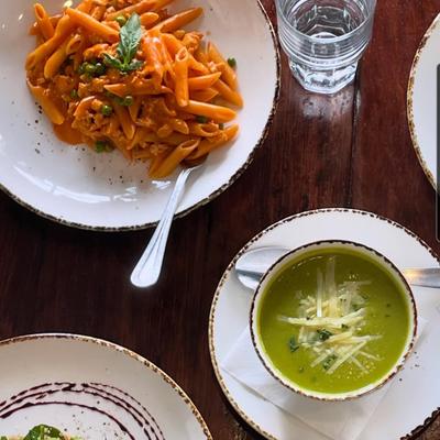 Penne pasta beside green soup on a wooden table, overhead view.