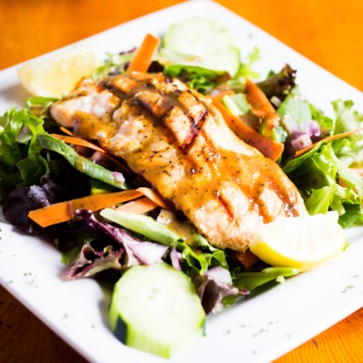 Filet of salmon over a bed of spring mix lettuce, red onion, tomato and cucumber
