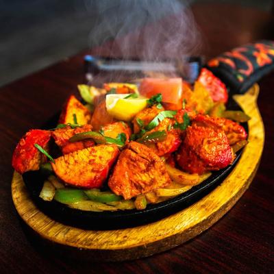 Marinated chicken pieces on a hot skillet with bell peppers and onions.