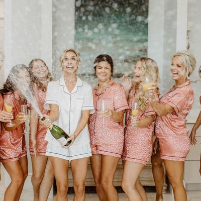 A joyful group of bridesmaids in matching pink pajamas are celebrating with champagne.