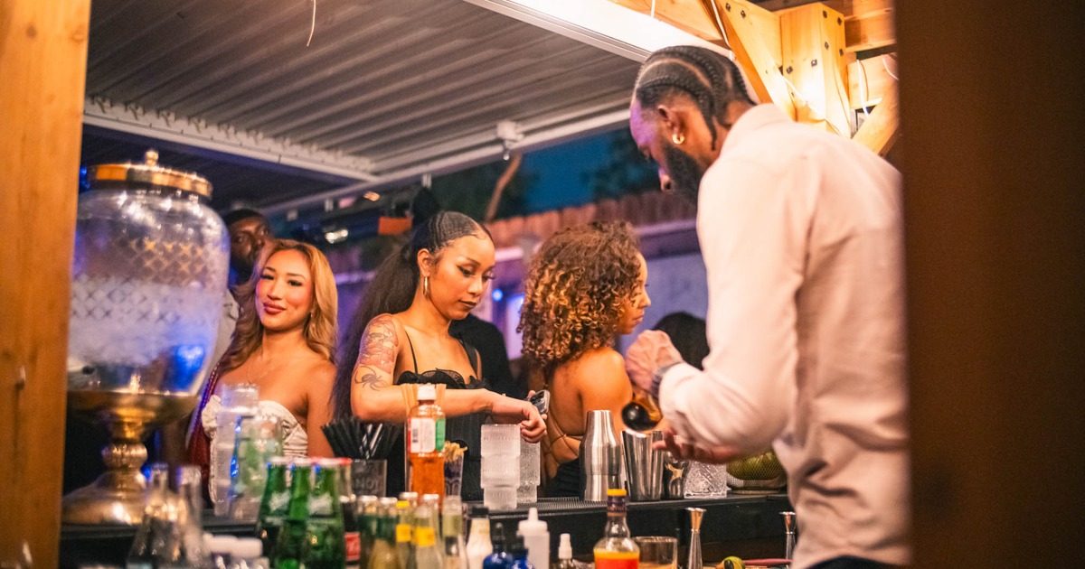 Outdoor bar with a bartender mixing drinks and patrons enjoying cocktails