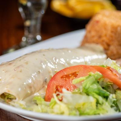 Grilled steak burrito topped with cheese sauce, served with rice, refreid beans, lettuce.