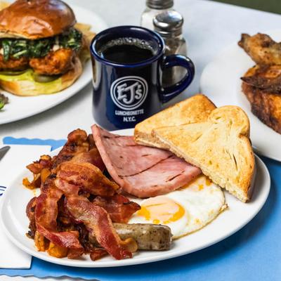 Breakfast sampler with two eggs, ham, smoked bacon, and sausage, served with coffee.