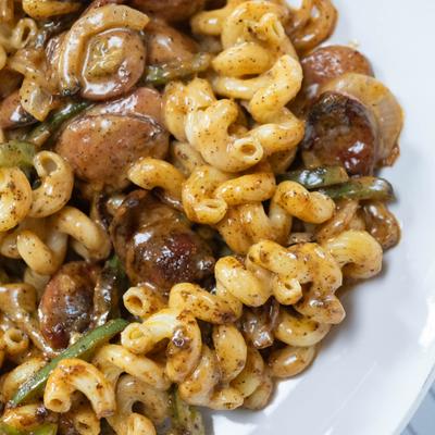 Pasta with sausage and vegetables on white plate.