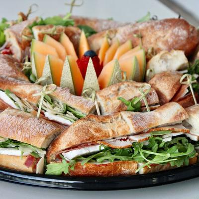 Prosciutto ham and cheese sandwiches with arugula, arranged on a platter with melon wedges