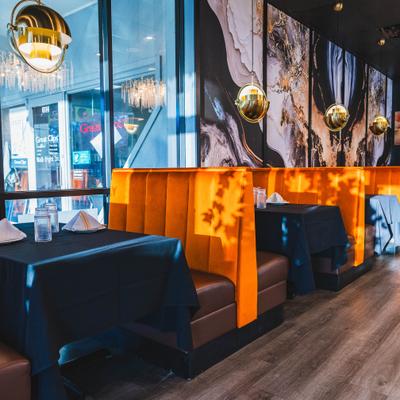 Modern restaurant with orange booths, black tables and spherical pendant lights..
