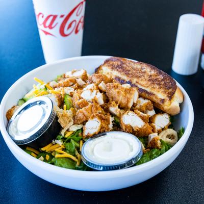 House Salad topped with fried chicken, alongside a drink.
